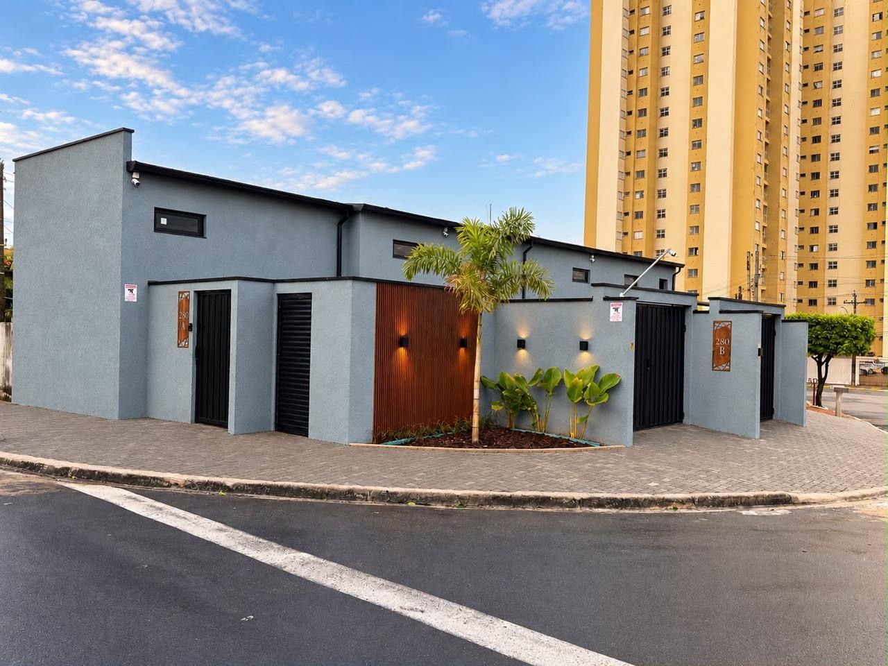 A modern building with a flat roof, a gated entrance, and a small garden area with plants.