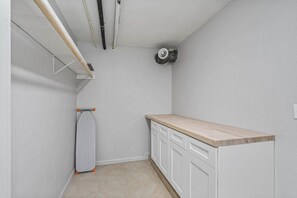 Een wasserette met een houten aanrechtblad, een hangende strijkijzer en een ventilatieopening in het plafond.