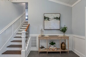 Een trap met witte leuningen en donkere treden, een bijzettafel met decoratieve objecten, en een lijst met een landschapschilderij aan de muur.