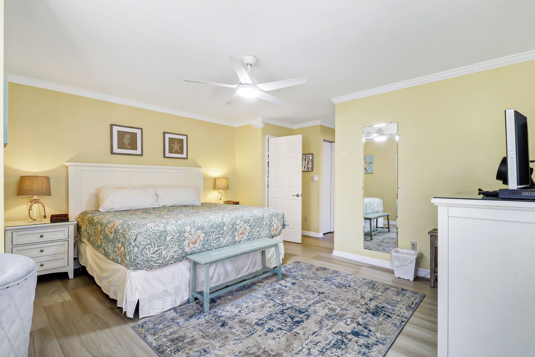 A bedroom with a bed, bedside tables, a ceiling fan, a mirror, a dresser, and a television.