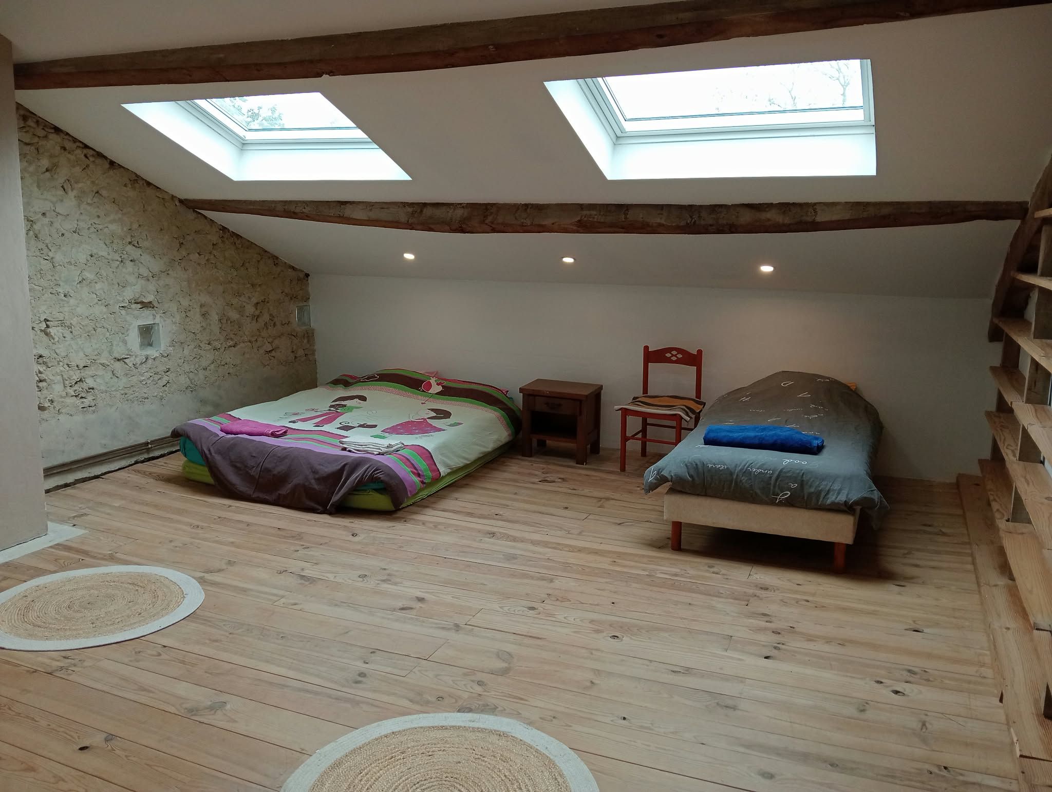 A loft bedroom with a sloped ceiling, skylights, a bed, a chair, and a small table.