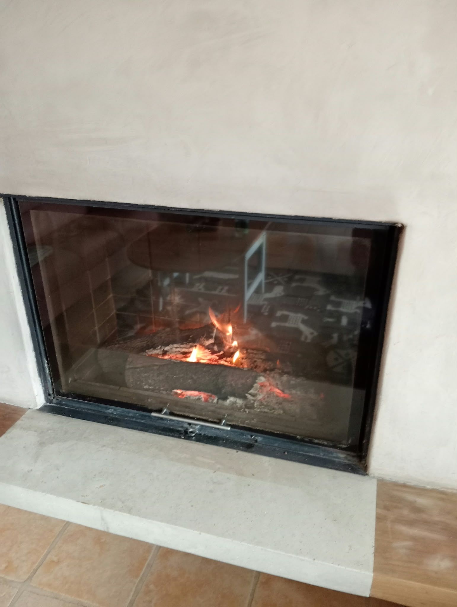 A fireplace with a glass front, a metal frame, and a tiled floor.