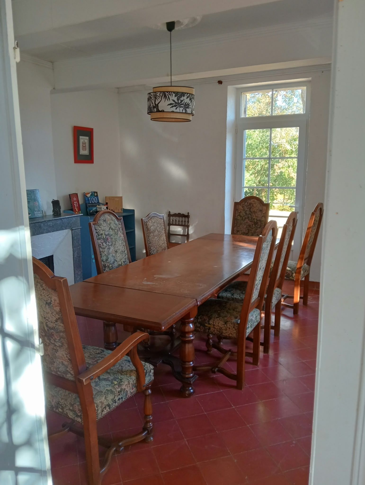Een eetruimte met een houten tafel en stoelen, een hanglamp en een raam met uitzicht op bomen.