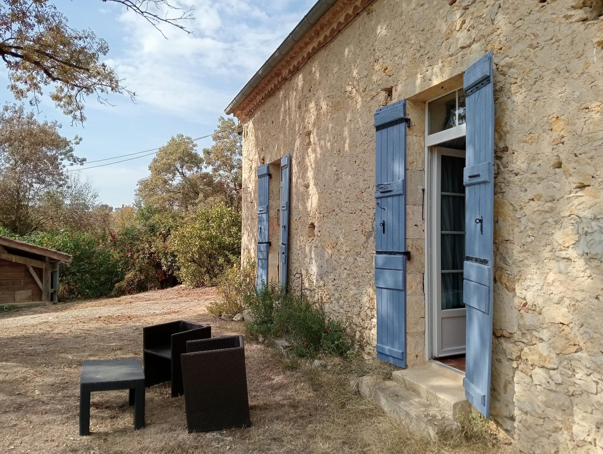 A stone building with blue shutters, a wooden bench, and a small table.