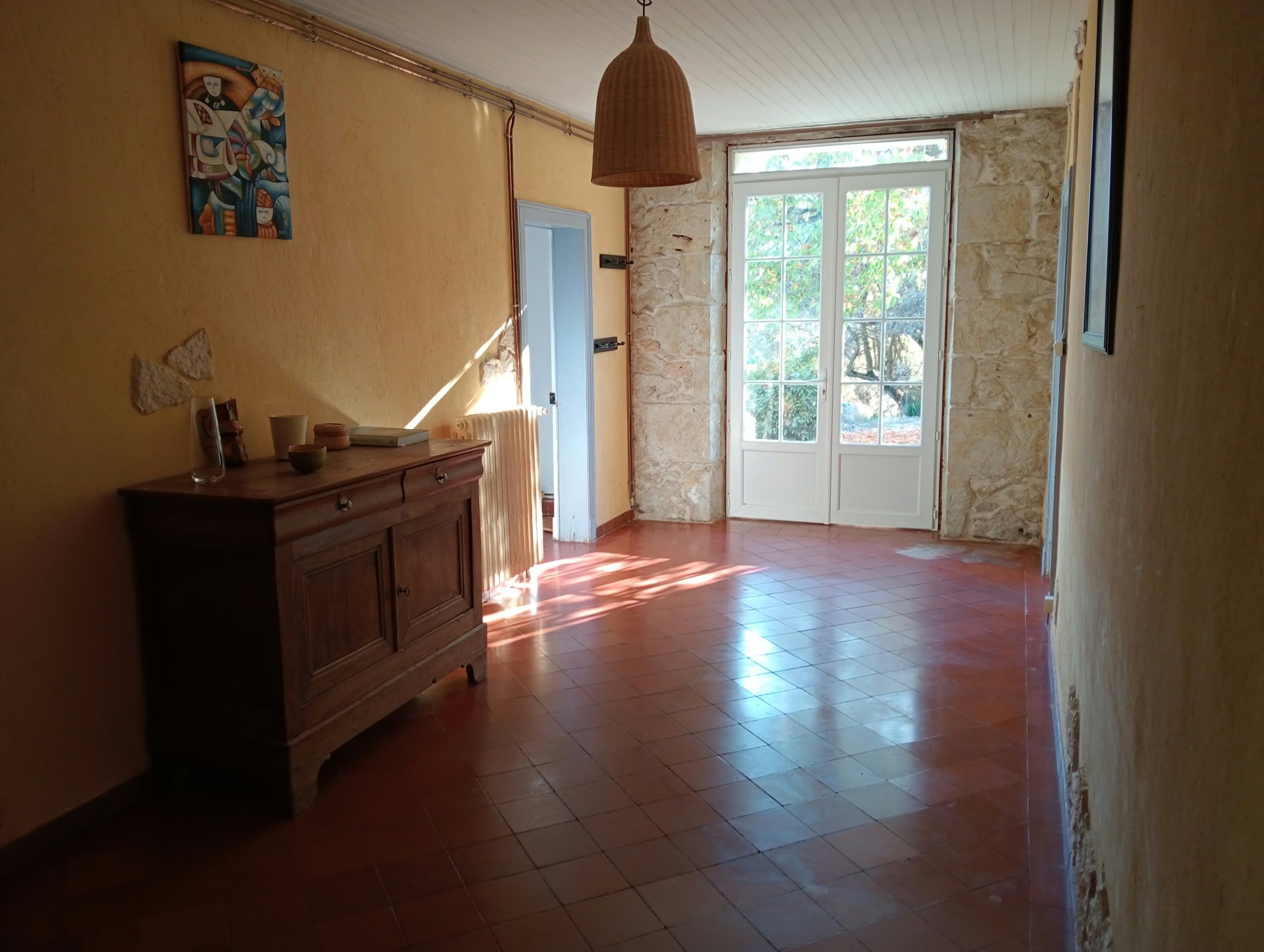 A spacious room with a wooden cabinet, a hanging light fixture, and a door leading to an outdoor area.