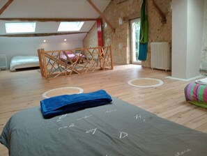 A room with a sloped ceiling, a bed with a blue blanket, a wooden gate, and a window with curtains. - New Listing (Sainte-Gemme)