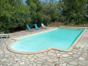 A rectangular swimming pool with a stone border, surrounded by a stone patio. There are two lounge chairs, one blue and one white, positioned near the pool. - New Listing (Sainte-Gemme)