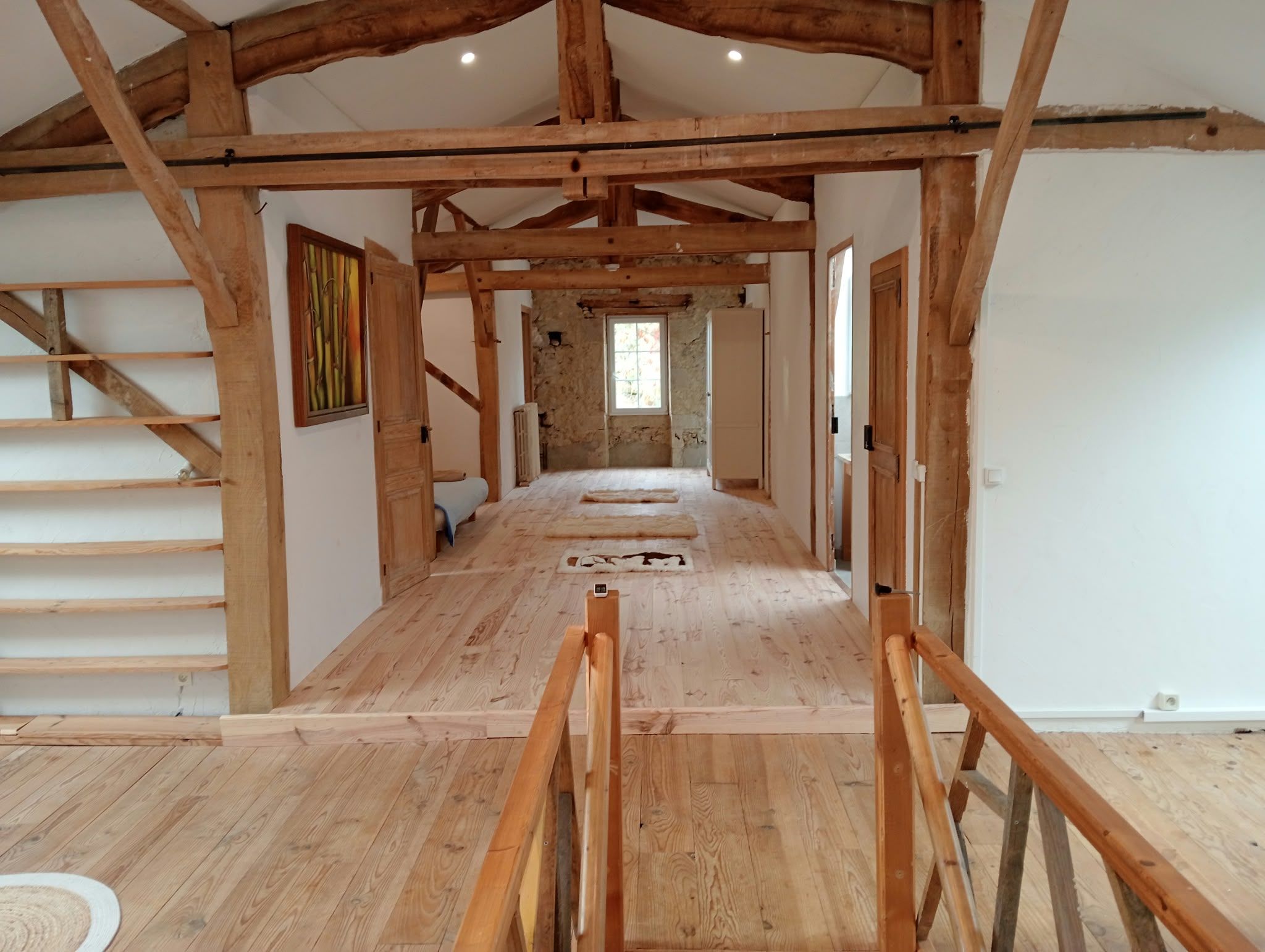 A spacious hallway with wooden beams, a staircase, and a window.