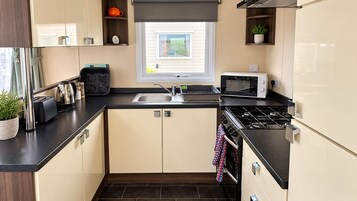 Une cuisine compacte équipée d’une cuisinière à gaz, d’un four à micro-ondes, d’un grille-pain et d’une fenêtre située au-dessus de l’évier.