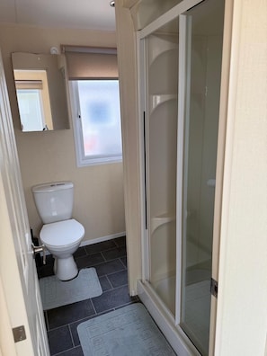 A bathroom with a toilet, a shower with a glass door, a window, and a towel rack.