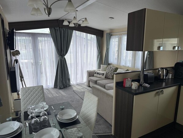 A modern hotel room with a dining area, a sofa with a 'SNUG' pillow, and a kitchenette.