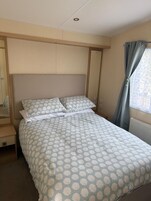 Ένα μονό κρεβάτι με ένα διακοσμητικό σεντόνι, ένα ξύλινο προσκέφαλο, ένα κομοδίνο και ένα παράθυρο με κουρτίνες.