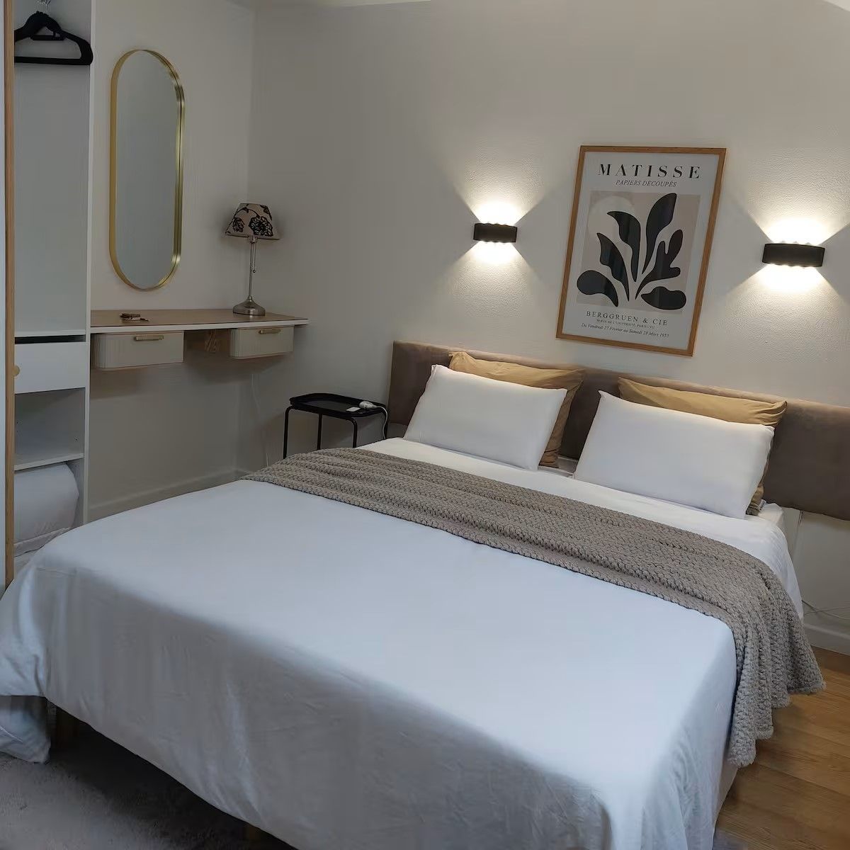 Ein ordentlich eingerichtetes Schlafzimmer mit einem Bett, Nachttischen, einer Lampe und Wandleuchten.