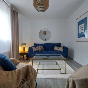 Een woonkamer met een blauwe bank, een glazen salontafel, een lamp en een ingelijst kunstwerk aan de muur.
