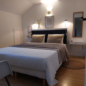 Een slaapkamer met een bed, nachtlampen, een nachtkastje, een spiegel en een aan de muur hangend kunstwerk.