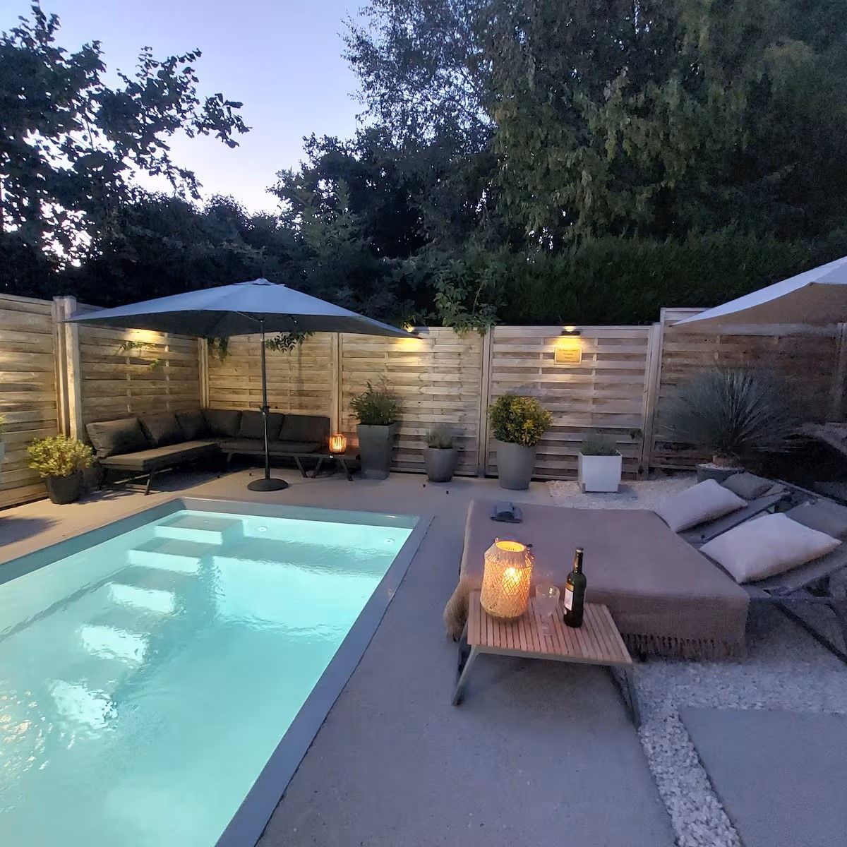 Ein Garten mit Schwimmbad, Sitzgelegenheit mit Kissen und Topfpflanzen.