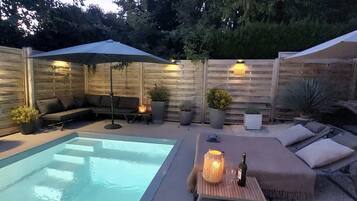 Ein Garten mit Schwimmbad, Sitzgelegenheit mit Kissen und Topfpflanzen.