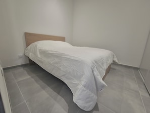 A small, single-bed room with a wooden headboard, white bedding, and grey tiled flooring. - Apartment with balcony near the sea, sleeps 4 (Toulon)