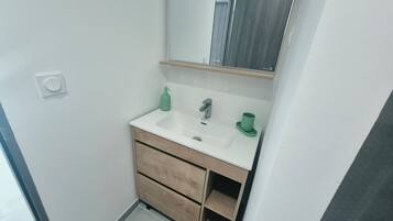 Un baño con un lavamanos blanco, un espejo y un dispensador de jabón verde.