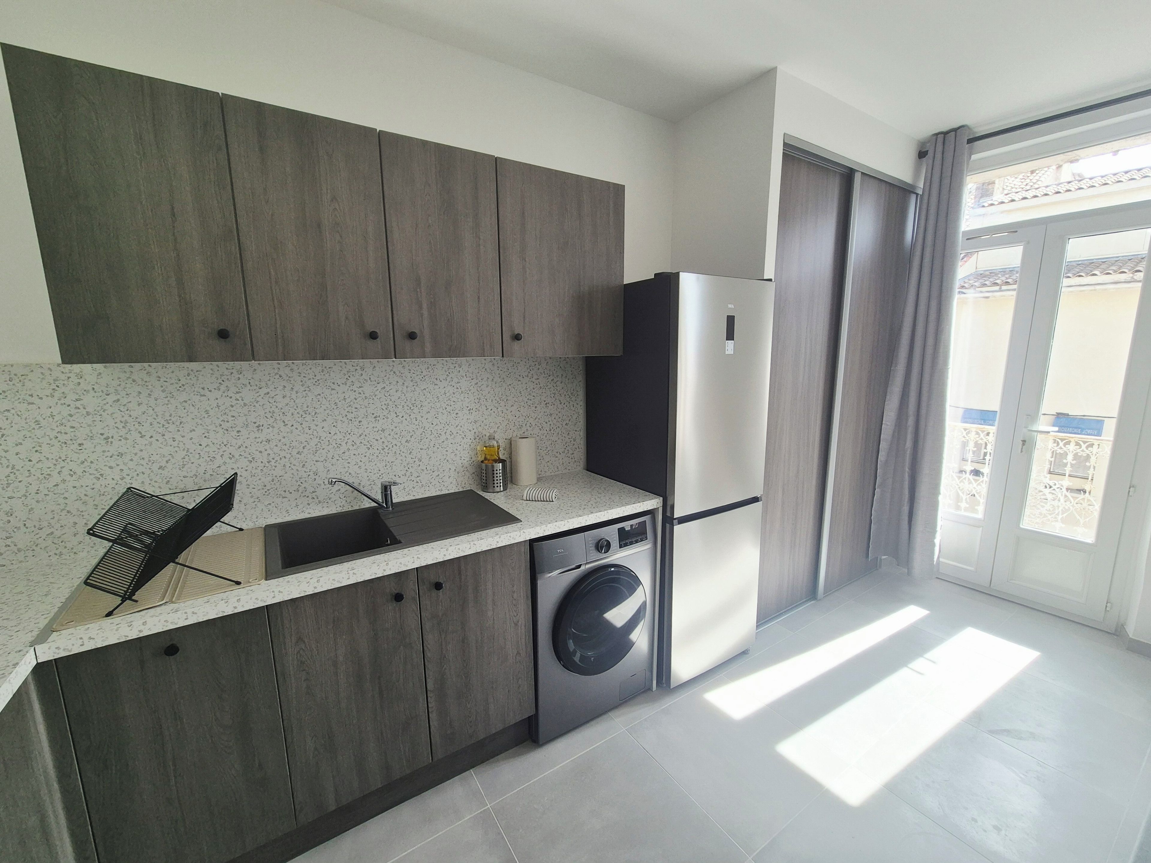 A modern kitchen with a built-in washing machine, a stainless steel refrigerator, and a window with a view.
