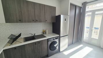 A modern kitchen with a built-in washing machine, a stainless steel refrigerator, and a window with a view.