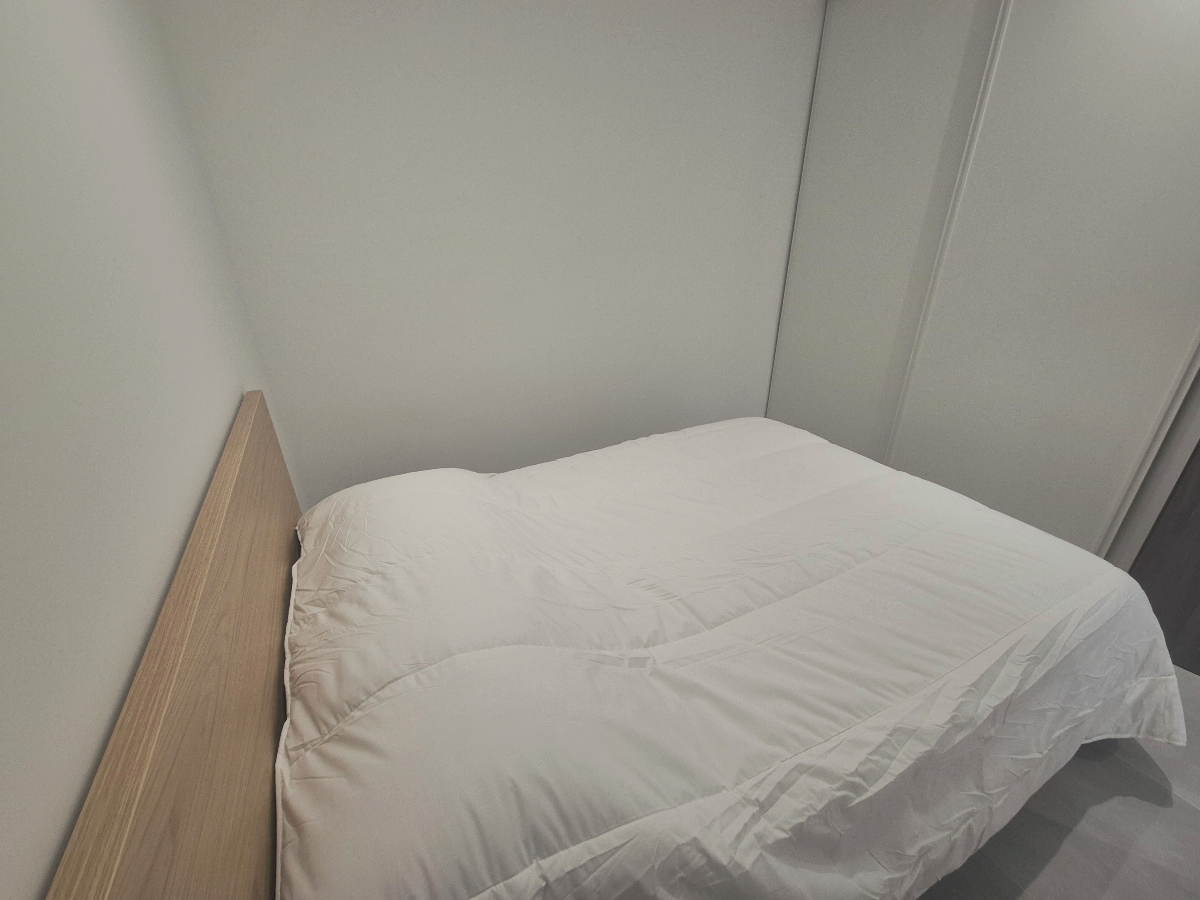 Un lit simple avec une tête de lit en bois, dans une pièce aux murs unis.
