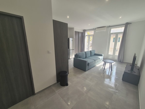 A modern living room with a grey sofa, a small round table, and a TV stand. - Apartment with balcony near the sea, sleeps 4 (Toulon)