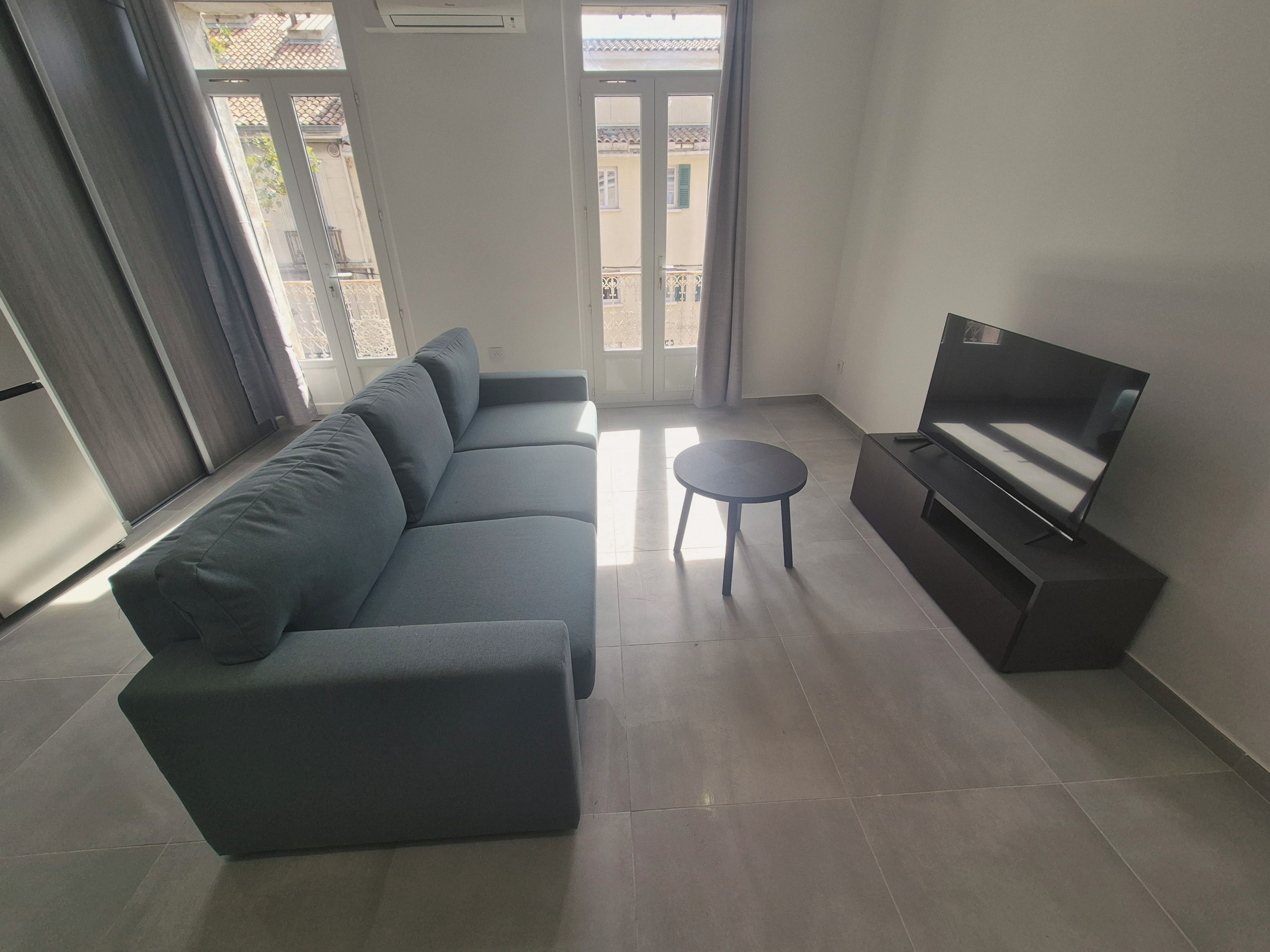Un salon moderne avec un canapé gris, une petite table ronde et un téléviseur à écran plat posé sur un meuble.