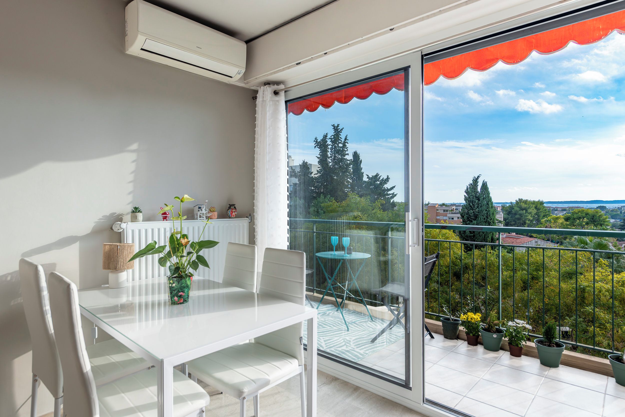 A balcony with a table and chairs, a potted plant, and a view of the cityscape.