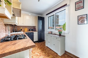A modern kitchen with a built-in stove, a refrigerator, and a window with a city view. - Bright apartment near the beaches of Juan-les-Pins (Antibes)