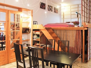 A cozy room with a wooden table, chairs, a bookshelf, and a loft bed with a red blanket. - Large, quiet apart with garden, close to transport (Ivry-sur-Seine)
