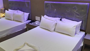Une chambre d’hôtel avec deux lits, chacun équipé de draps et d’oreillers blancs, une table de chevet avec une lampe et une prise électrique.