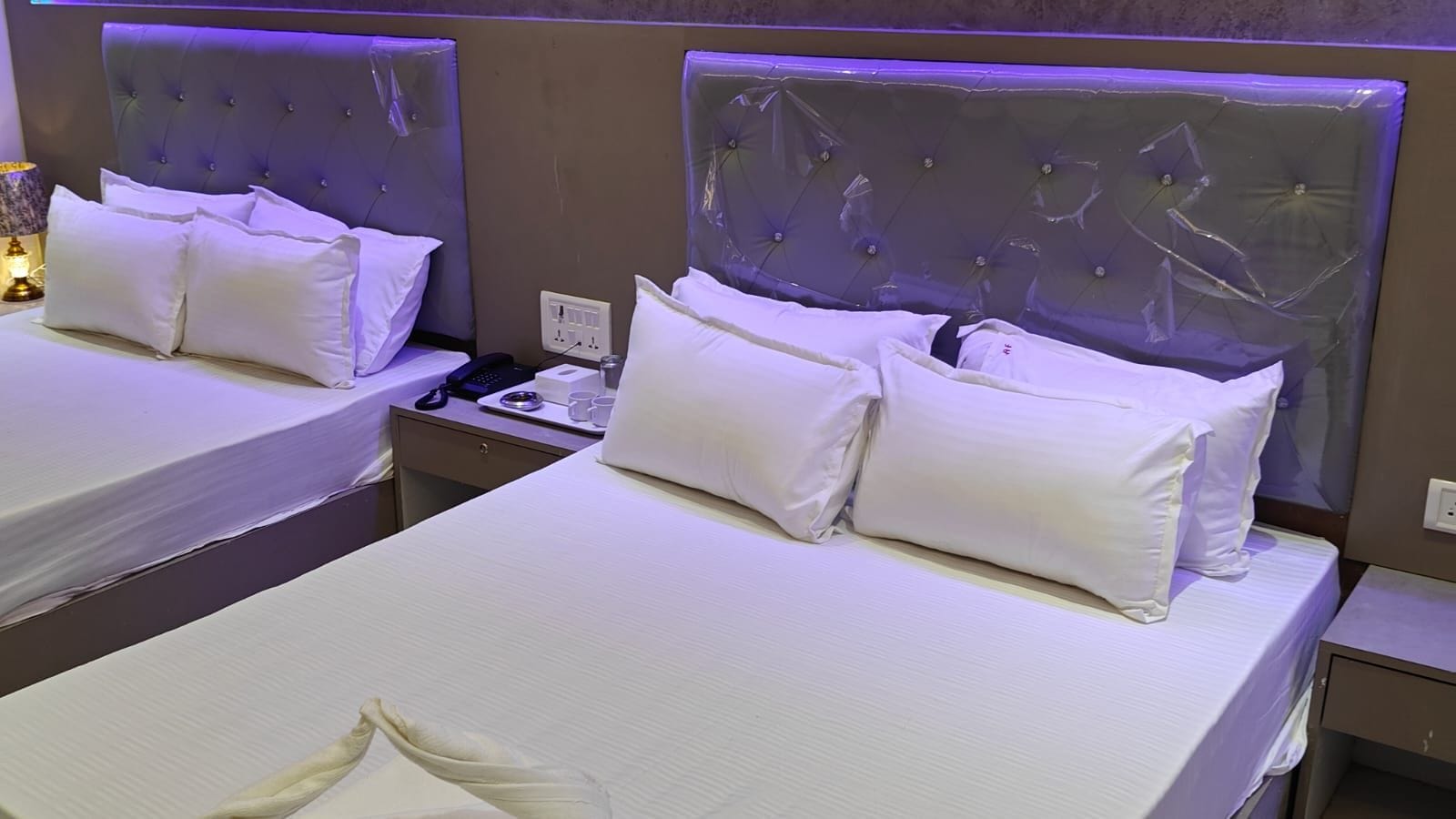 Habitación de hotel con dos camas, cada una con sábanas y almohadas blancas, y una mesita de noche con un teléfono y una taza.