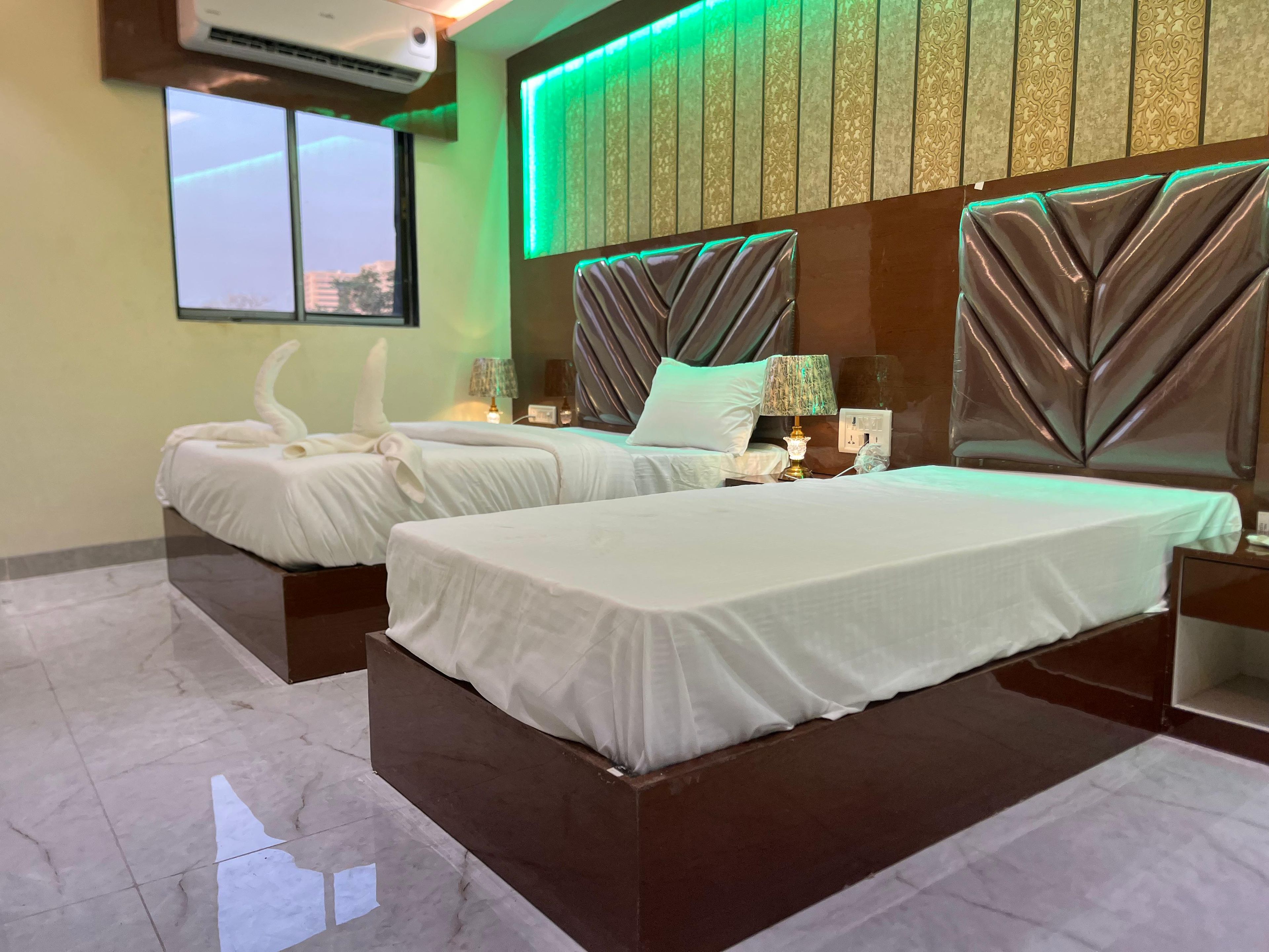 Habitación de hotel con dos camas, un ventanal grande y una pared iluminada en verde.