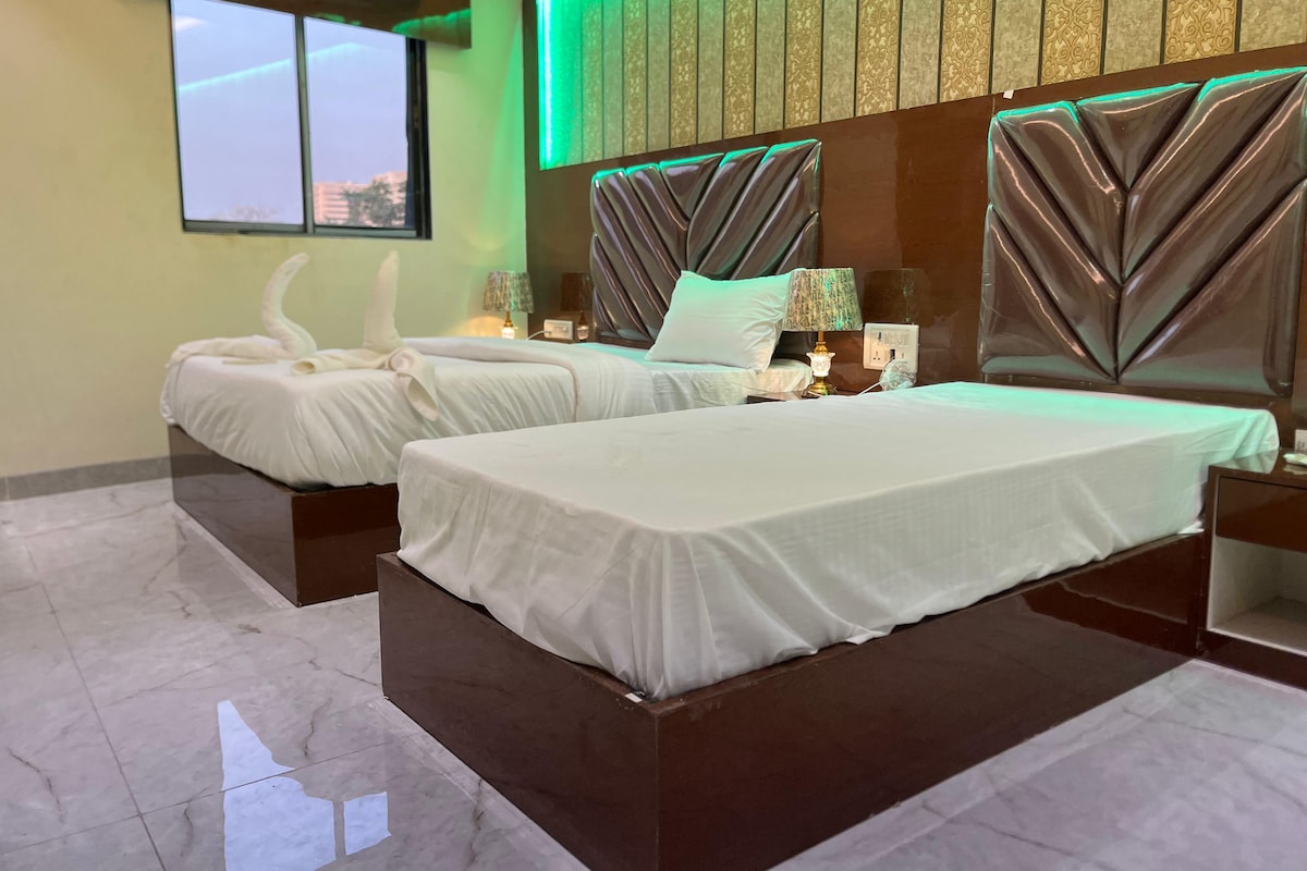 Une chambre d’hôtel avec deux lits, une grande fenêtre et un mur éclairé en vert.
