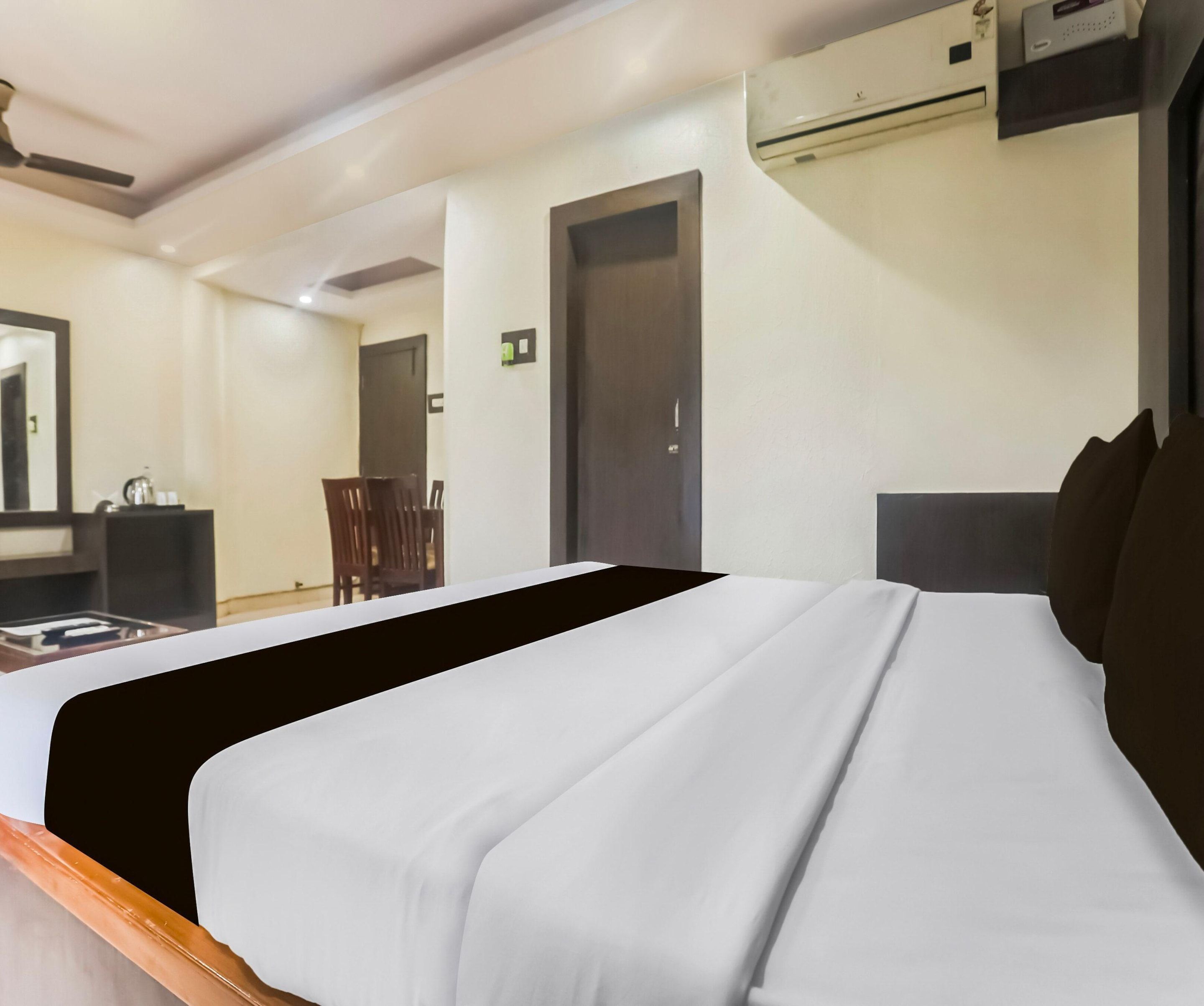 A hotel room with a bed, a desk, a chair, and an air conditioning unit.