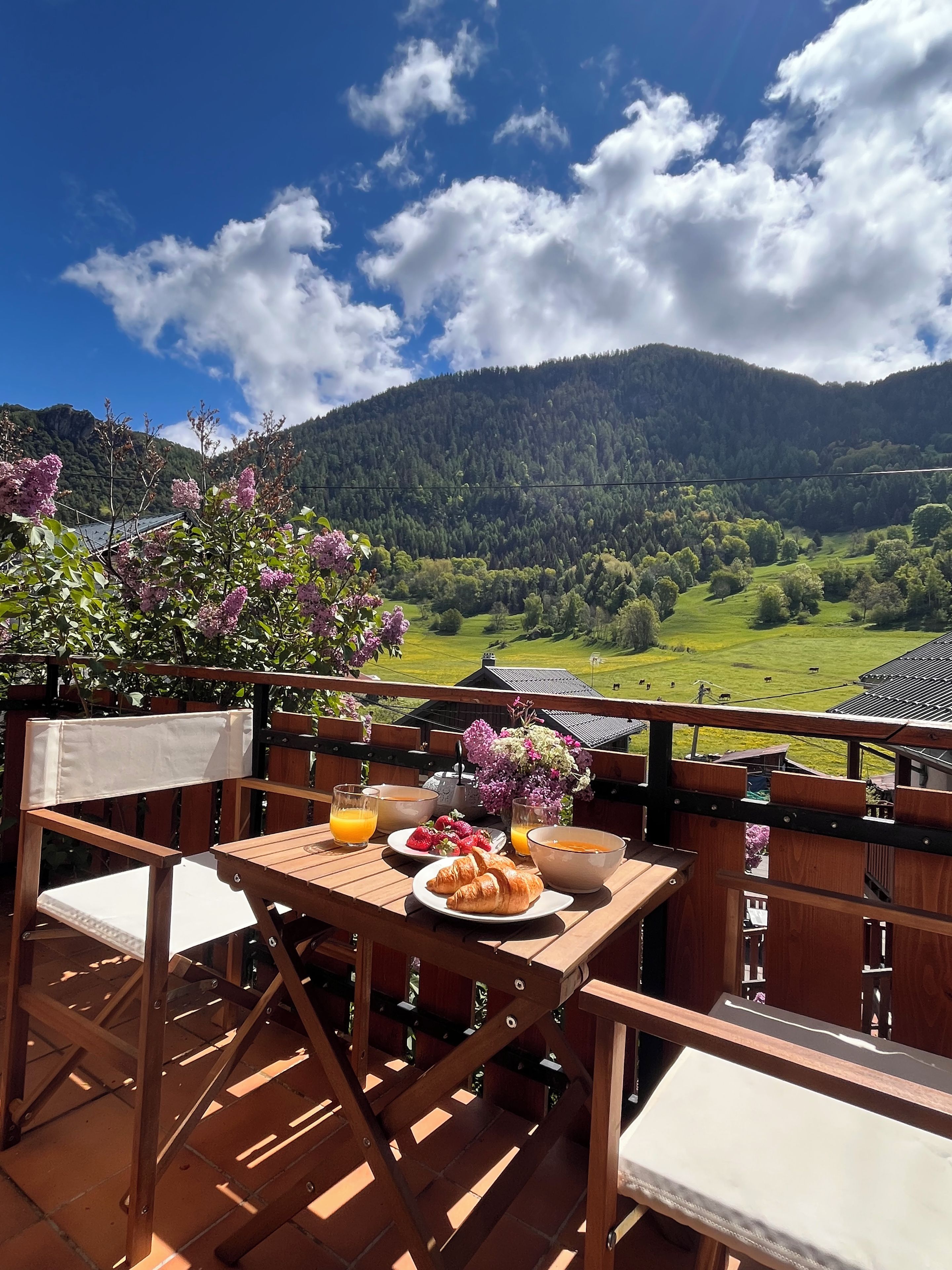 A wooden deck with a table set for breakfast, overlooking a mountainous landscape.