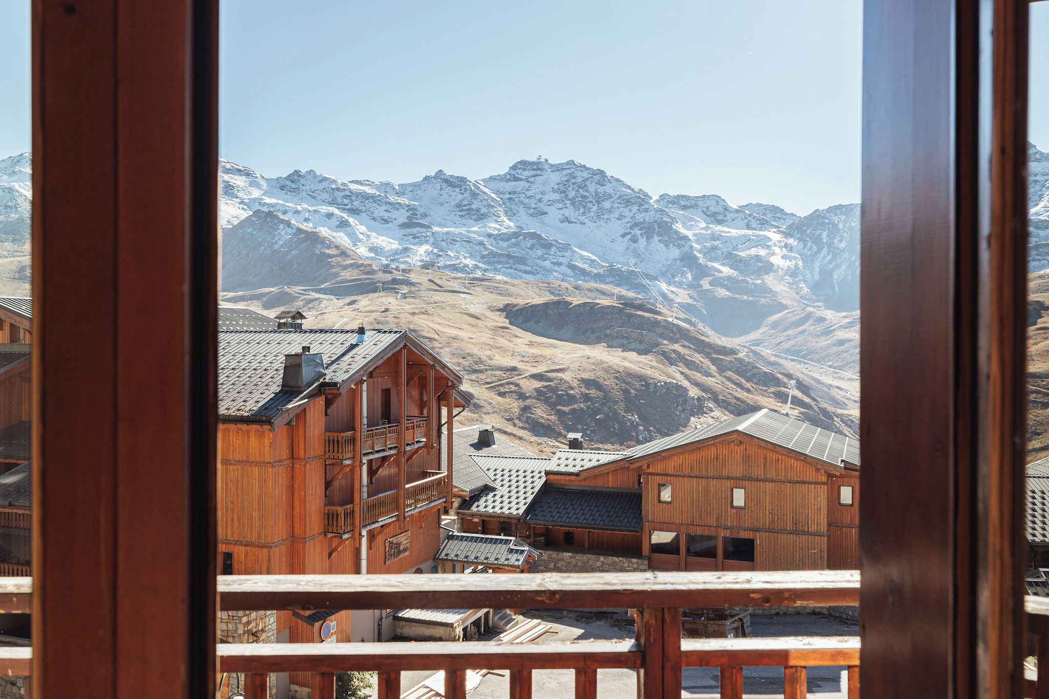A wooden building with a balcony, set against a backdrop of snow-covered mountains.