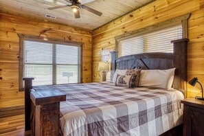 Ein Schlafzimmer einer Holzhütte mit einem Bett, einem Nachttisch, einer Lampe und einem Deckenventilator.