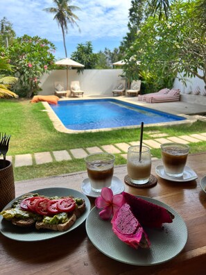 A dining table with a meal, drinks, and a view of a swimming pool.