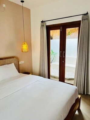 Ein Hotelzimmer mit einem Bett, einer Hängelampe, einer Schiebetür aus Glas und Blick auf einen Garten.