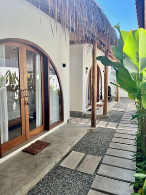 A modern building with a curved glass door, a thatched roof, and a gravel pathway. - Villa Mila Gili Air (Pemenang Kabupaten Lombok Utara)
