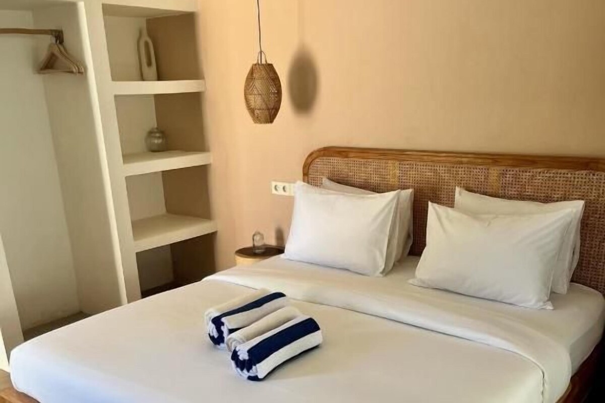 A bedroom with a wooden bed frame, white bedding, and a bedside table with a lamp.
