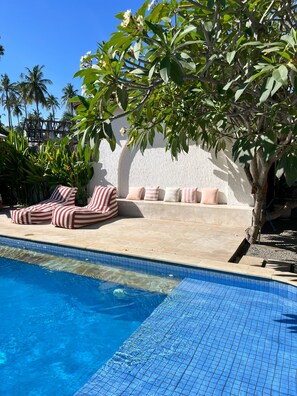 Un espace piscine avec des chaises longues et un coin salon doté de coussins.