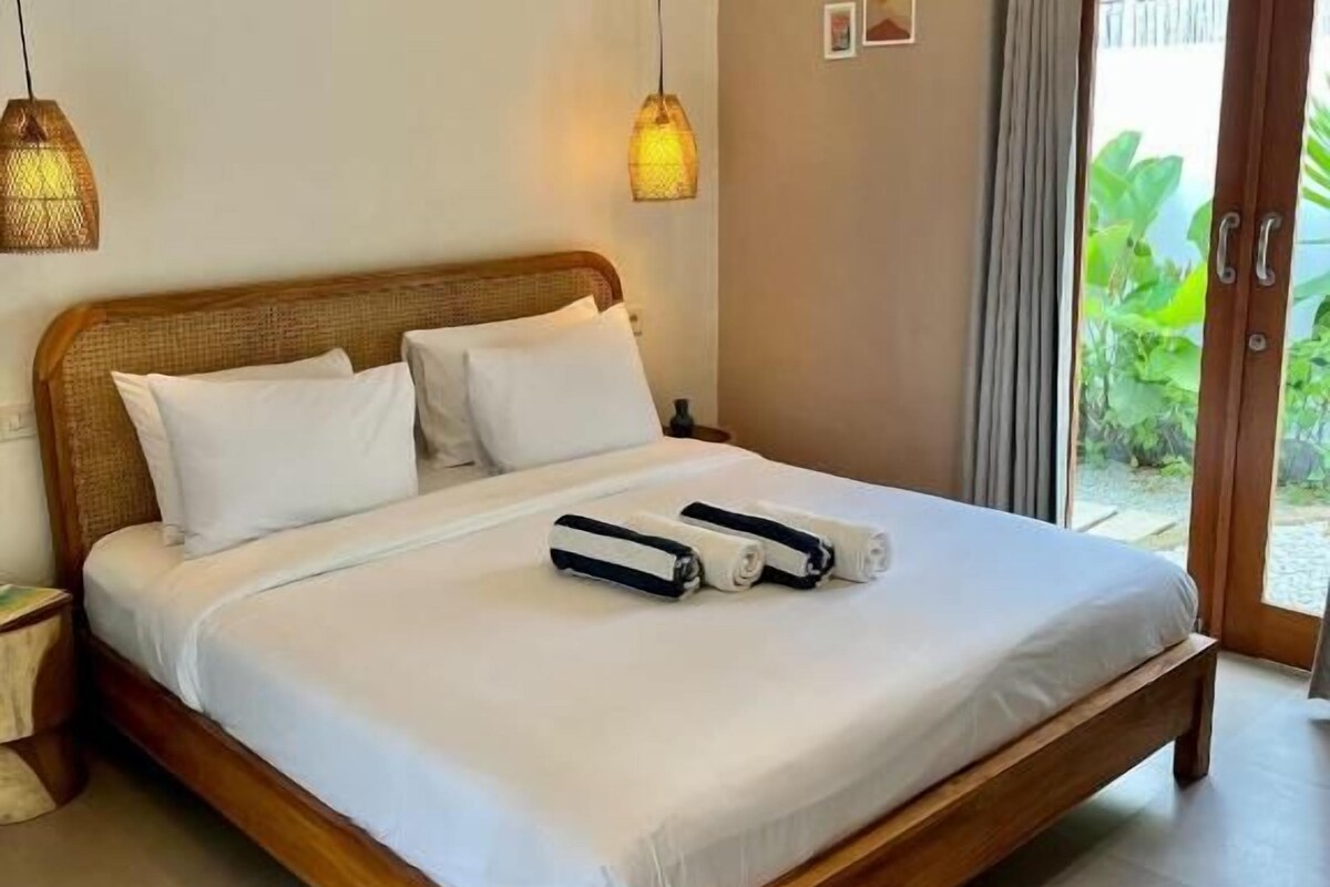 Une chambre à coucher avec un lit en bois, du linge de lit blanc et deux lampes suspendues.
