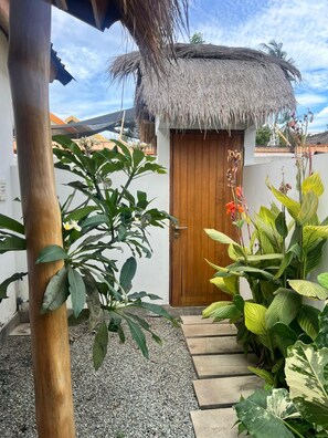 A thatched-roof structure, a wooden door, and various tropical plants.
