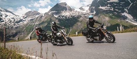Two motorcyclists on a road with a mountainous backdrop.