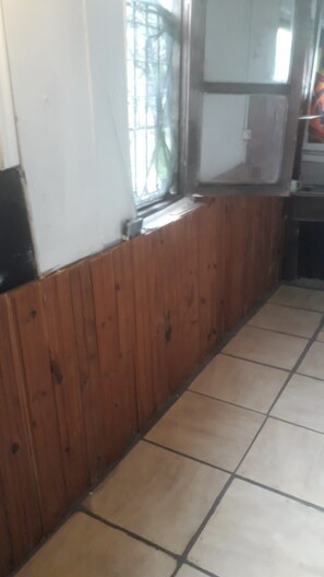 Um quarto com parede de painel de madeira, piso ladrilhado e janela com barras de metal.