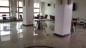 Un hall d’hôtel spacieux, doté de plusieurs espaces de détente, d’un sol en marbre poli et de grandes fenêtres laissant entrer la lumière naturelle.