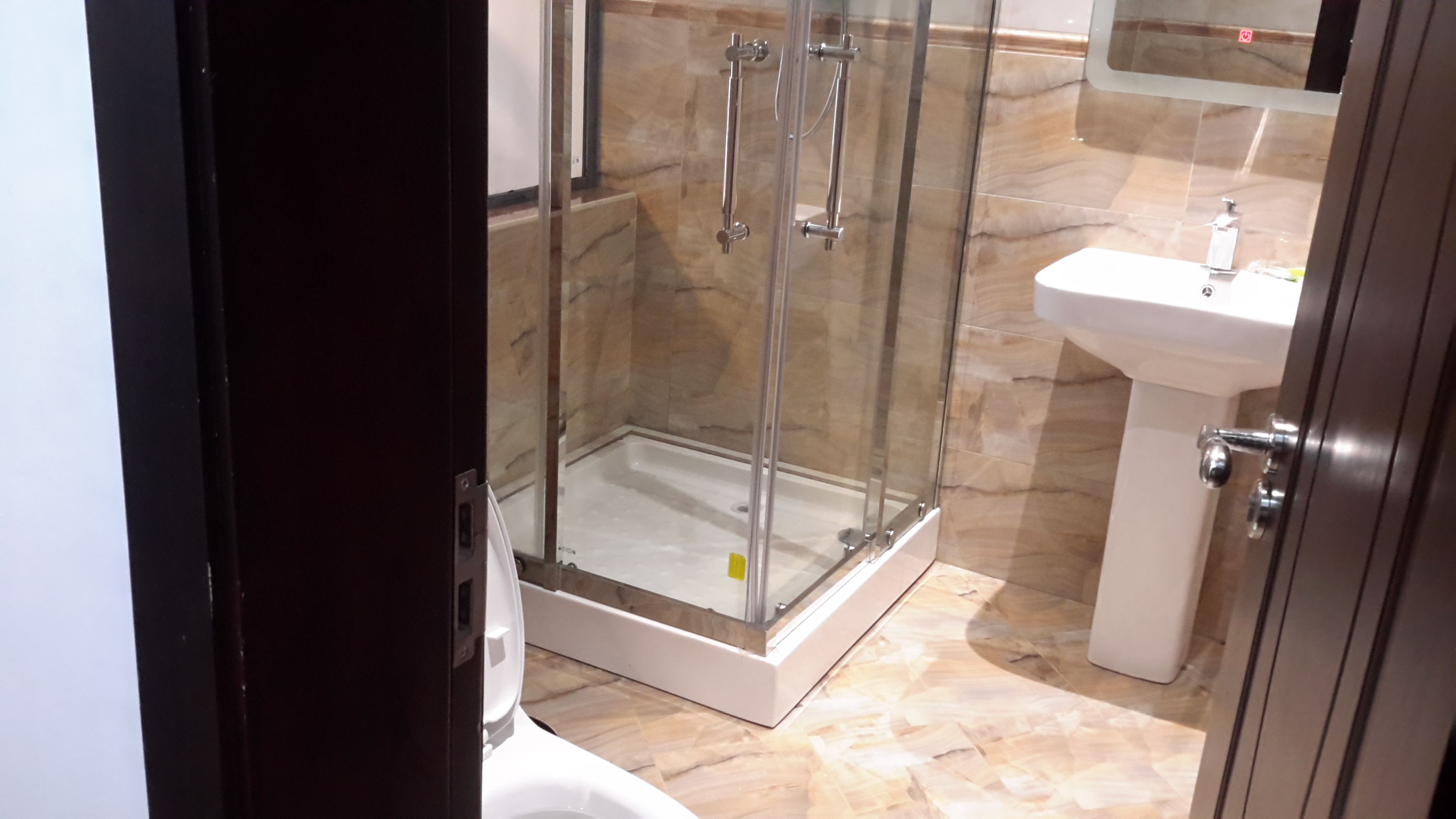 Une salle de bain dotée d’une douche à parois de verre, d’un lavabo blanc et d’un sol carrelé en marbre.